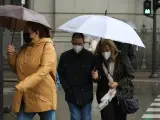 Transeúntes caminan en Madrid protegiéndose de la lluvia con paraguas.