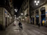 Un repartidor de comida a domicilio circula con su bicicleta por una calle vacía del centro de Barcelona, la primera noche con toque de queda en la ciudad.