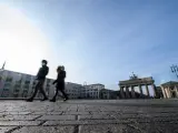 Dos transeúntes con mascarilla cruzan junto a una desierta Puerta de Brandenburgo en Berlín.