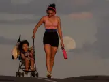 Una madre lleva a su hijo en un carrito, con la superluna de fresa al fondo, mientras pasea por una calle de Los Ángeles (EE UU).