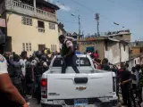 Decenas de personas se arremolinan en torno a un vehículo policial en el que son custodiados dos extranjeros, en Puerto Principe (Haití), tras el asesinato del presidente del país, Jovenel Moise.