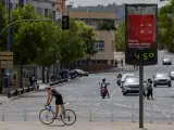 Un joven en bicicleta pasa junto a un termómetro que marca 45 grados centígrados en Sevilla.