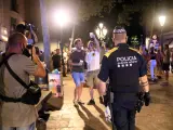 Un agente de la Guardia Urbana de Barcelona delante de personas haciendo botell&oacute;n, este s&aacute;bado.