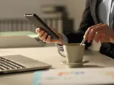 Una persona mira su móvil mientras se toma un café y trabaja.