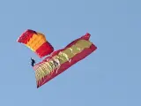 Un paracaidista de la Patrulla Acrobática traslada la bandera tras saltar de un avión sobre el Paseo de la Castellana.