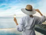 Una mujer en bata de baño blanca sostitne una copa de champán en la mano mirando al mar