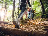Hiker woman with trekking sticks climbs steep on mountain trail, focus on boot