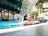 Mujer disfruta de los tratamientos del spa bajo el arroyo de agua en la piscina.