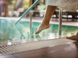Mujer en bata de baño sumergiendo los pies en la piscina.