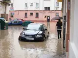 Una persona camina por una calle llena de coches rodeados de agua en Pamplona (Navarra).