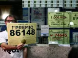 El propietario de la administración de la Estación de Atocha, en Madrid, muestra el 86148 que ha sido agraciado con el primer premio de la Lotería de Navidad 2021.