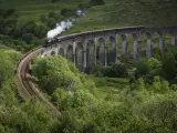 'The Jacobite', el tren de vapor histórico cruza los icónicos arcos del viaducto de Glenfinnan sobre una cañada de montaña verde en las profundidades de las Tierras Altas de Escocia, Reino Unido.