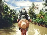 Mujer viajera con mochila parada cerca de un gran r&iacute;o tropical en un d&iacute;a soleado Una mujer viajera parada frente al r&iacute;o Kapuas en Indonesia.
