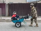 Un hombre mayor es transportado, en carretilla, por un soldado ucraniano.