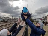 Oleg (derecha), que decidió permanecer en Irpin, pasa a su hijo Maksim por encima de una valla a su esposa Yana, antes de la llegada de un tren de evacuación a la ciudad de Kiev (Kiev), en la estación de tren de Irpin, Ucrania.