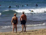 Una pareja de turistas observa cómo varios jóvenes toman clases de surf este jueves santo en la playa de Maspalomas, en Canarias.