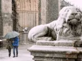 Dos personas se protegen de la nieve junto a los leones de la catedral de Ávila.