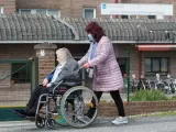Una mujer traslada a una mujer de avanzada edad en silla de ruedas frente a la Residencia de Mayores As Gándaras (Lugo).