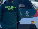 Imagen de archivo de un agente de la Guardia Civil de espaldas y junto a un vehículo oficial del cuerpo.