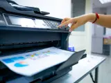 Office worker prints paper on multifunction laser printer. Copy, print, scan, and fax machine in office. Document and paper work. Print technology. Hand press on photocopy machine. Scanner equipment