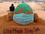 Escultura de arena del globo terráqueo con mascarilla y la palabra "ómicron" escrita sobre el mundo.