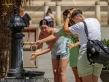 Unas turistas se refrescan en una fuente de agua junto a la Catedral de Sevilla.