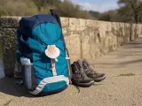 Backpack with seashell symbol of Camino de Santiago, trekking boots and poles leaning on stone wall. Pilgrimage to Santiago de Compostela. Copy space