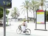 Una mujer en bicicleta por Sevilla junto a un termómetro que marca 45 grados.