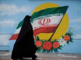 Una mujer con chador camina junto a un mural con la bandera de Irán en Teherán