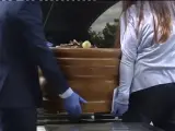 Personas introduciendo un ataúd en un vehículo funerario.