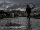 Una mujer se refugia de la lluvia con un paraguas mientras camina por el puente romano de Ourense.