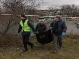 Forenses y policías transportan en una bolsa restos humanos hallados en una fosa común en la localidad de Pravdyne, en las afueras de Jersón, Ucrania.