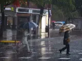Dos mujeres cruzan bajo un paraguas un paso de peatones tras las fuertes lluvias en el puente del mes de diciembre en Sevilla