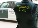 Un agente de la Guardia Civil, de espaldas, junto a un vehículo oficial..