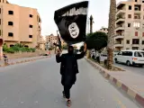 Persona levantando un arma y la bandera del Estado Islámico (archivo).