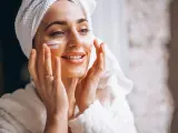 Mujer aplicándose crema facial frente al espejo.