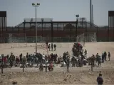 Migrantes esperan a las autoridades estadounidenses, entre una barrera de alambre de púas y la valla fronteriza en la frontera entre Estados Unidos y México, visto desde Ciudad Juárez, México.