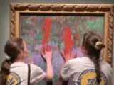 Momento en el que las activistas del movimiento climático Restaurar Humedales manchan de pintura roja el cuadro de Monet, El jardín del artista en Giverny, y se pegan a él, en el Museo Nacional de Estocolmo. Europa Press.