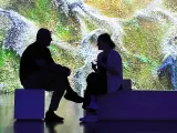 Dos personas sentadas ante una pieza de la exposición 'Digital impact'.