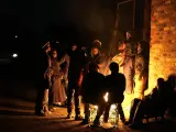 Varias personas se apiñan alrededor de una hoguera para calentarse en el asentamiento informal de Angelo, en Boksburg, Sudáfrica, el jueves 6 de julio de 2023. La policía informó de que una fuga de gas causó la muerte de varias personas, entre ellas varios niños.