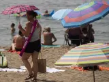 Una mujer con una sombrilla camina buscando sitio en la playa.