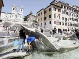 Un par de jóvenes se refrescan con cubos de agua en una fuente de Piazza Spagna en Roma.