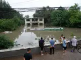 Esta foto tomada el 31 de julio de 2023 muestra a la gente mirando un edificio parcialmente sumergido en una zona inundada, tras las fuertes lluvias en el distrito de Fangshan, en Pekín. La tormenta Doksuri, un antiguo supertifón, se ha extendido hacia el norte sobre China desde el viernes.