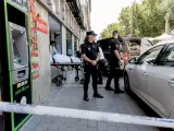Dos agentes de Policía Nacional mientras los trabajadores de Interfunerarias se llevan el cuerpo de la dueña de la tienda de ropa de trabajo 'Vistebien'.