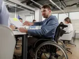 Happy businessman in a wheelchair talking to his colleague about reports on a meeting in the office.