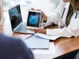 Unrecognizable female doctor shows a male patient an image of his brain from an MRI scan. The image is on a digital tablet.