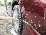 Un conductor limpia las llantas de su coche con jabón