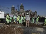 Trabajadores municipales remueven montones de tierra que simbolizan fosas clandestinas que fueron colocadas por personas que tienen familiares desaparecidos que exigen respuestas al gobierno afuera del Palacio Nacional en la Ciudad de México.