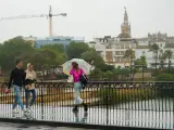 Varias personas caminan por el Puente de Triana bajo las últimas lluvias registradas en Sevilla.