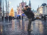 Portrait of young couple in the old city center on cold winter day. Man is holding woman in the air while they are kissing. They are happy together. People and city with christas lights in back, defocused.